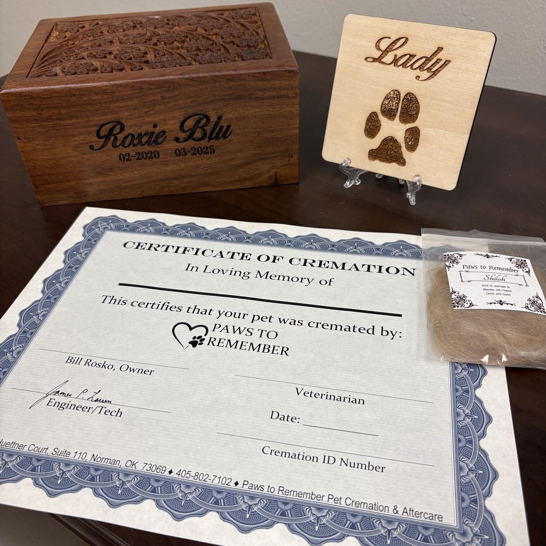 premium package contents: a carved wooden box for the cremains, a wooden paw print keepsake, a certificate, and a bagged clipping of hair