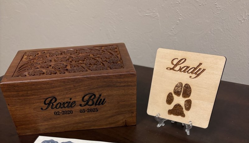 premium package contents: a carved wooden box for the cremains, a wooden paw print keepsake, a certificate, and a bagged clipping of hair