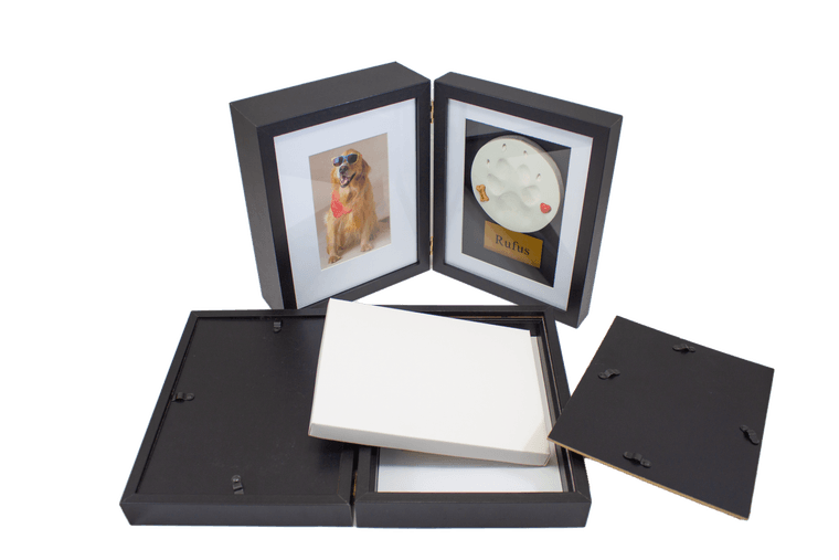 a hinged black shadowbox frame with a dog's photo on one side and a cast paw print with an engraved nameplate on the other