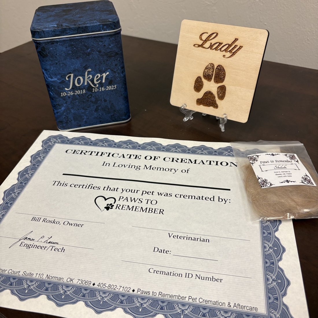 standard package contents: an engraved metal box for the cremains, a wooden paw print keepsake, a certificate, and a bagged clipping of hair